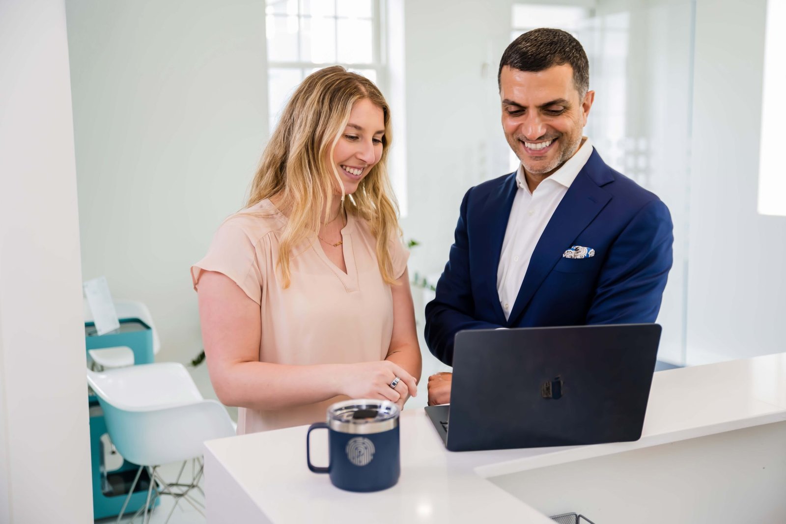 Two professionals in a modern clinic setting collaborate and review something on a laptop, highlighting teamwork, communication, and training often found in high-performing chiropractic teams. The scene is bright, wide, and inviting, conveying operational excellence and a seamless patient experience.