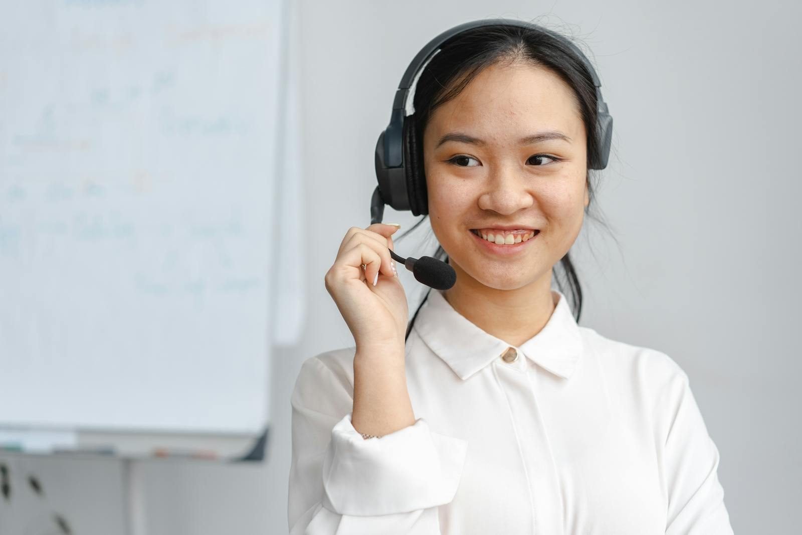 Asian woman smiling in a customer service role wearing a headset indoors.